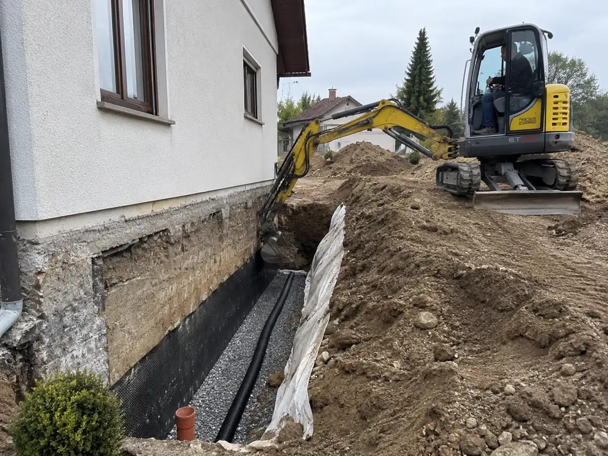 Hauseigener Bagger legt das Fundament frei – Drainage-Rohr, Kies und Noppenbahn bereits verlegt